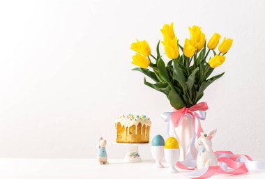 Şenlikli iç mekan, vazoda sarı laleler ve paskalya yumurtaları, sevimli tavşanlar ve Paskalya pastası.