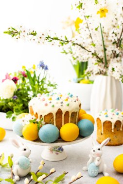 Paskalya Evi 'nin içi, vazonun arka planında yumurtalar, çiçek açan kiraz dalları ve buketler dolusu çiçekler, sevimli tavşanlar olan Paskalya pastası.
