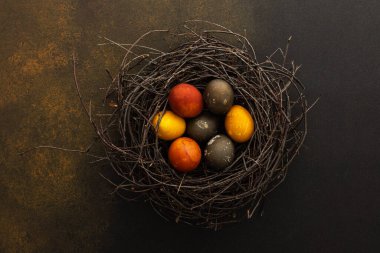 Kahverengi arkaplanda bir yuvadaki renkli Paskalya yumurtaları, üst görünüm, boşluğu kopyala