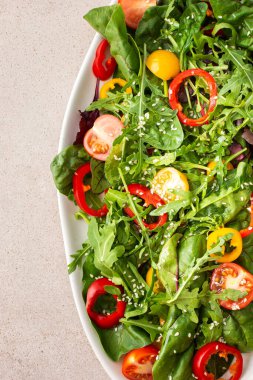 Pembe arka planda oval bir tabakta taze çiftlik sebzeleri salatası, sitya marul ve bahçe, domates ve renkli dolma biber, roka ve susam tohumları.