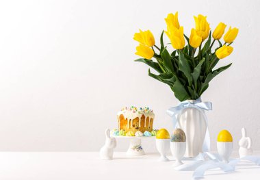 Şenlikli iç mekan, vazoda sarı laleler ve paskalya yumurtaları, sevimli tavşanlar ve Paskalya pastası.