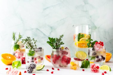 Refreshing drinks with ice cubes with fruits , ice with blackberries and raspberries, gooseberries and currants, with mint, a jug of water and citrus fruits