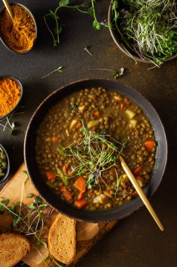 Sağlıklı vejetaryen yemekleri, domatesli kahverengi mercimek çorbası, havuç, patates ve köri baharatı, kızarmış ekmek, kahverengi arka planda kesme tahtasında çorba.