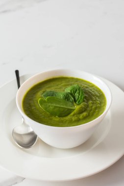 Sağlıklı kahvaltı, yeşil brokoli ve beyaz kasede ıspanak kremalı çorba mermer arka planda gri peçeteli, üst manzaralı.