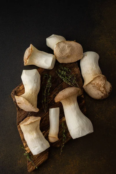 Stock image Pleurotus eryngii mushrooms on a cutting board with thyme on a brown background, tasty healthy mushrooms, top view