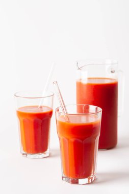 Bardakta taze sıkılmış domates suyu ve beyaz arka planda bir sürahi.