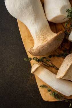 Kahverengi arka planda kekik olan kesme tahtasındaki Pleurotus eryngii mantarları. Lezzetli, sağlıklı mantarlar. Yakın plan.