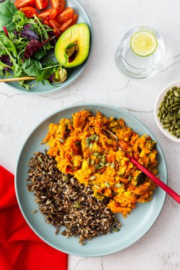 Healthy lunches, wild rice with carrot and tomato gravy, broccoli and onion, fresh mixed salad with pumpkin seeds, water with lemon, top view