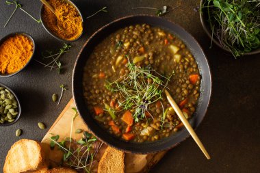 Healthy vegetarian lunches, brown lentil soup with tomatoes and carrots, potatoes and curry spices, toasted croutons, bowl with soup on cutting board on brown background clipart