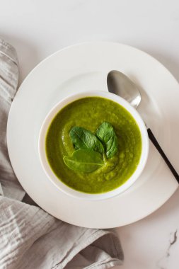 Sağlıklı kahvaltı, yeşil brokoli ve beyaz kasede ıspanak kremalı çorba mermer arka planda gri peçeteli, üst manzaralı.