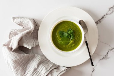 Sağlıklı kahvaltı, yeşil brokoli ve beyaz kasede ıspanak kremalı çorba mermer arka planda gri peçeteli, üst manzaralı.