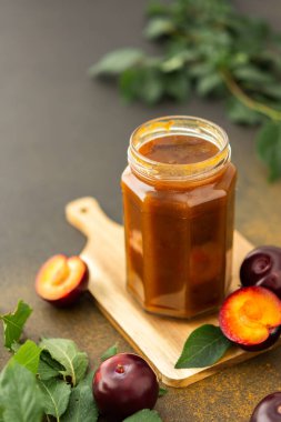 Homemade plum jam in a jar on a board with fresh plums, harvesting for the winter