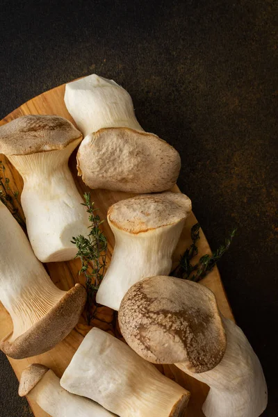 stock image Pleurotus eryngii mushrooms on a cutting board with thyme on a brown background, tasty healthy mushrooms, top view