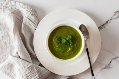 Sağlıklı kahvaltı, yeşil brokoli ve beyaz kasede ıspanak kremalı çorba mermer arka planda gri peçeteli, üst manzaralı.