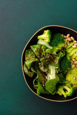 Sağlıklı kahvaltı, fasulye, salatalık, avokado ve brokoli serpiştirilmiş yeşil arka planda bir tabak yemek.