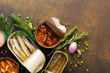 Baharat ve bitkilerin arasında farklı teneke kutular, kahverengi bir arka planda konserve somon ve uskumru, sprat ve sardalya, ton balığı ve ringa balığı ve balık ezmesi.