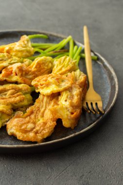 Kızarmış kabak çiçekleri hamurda, kabak çiçekli bir tabak koyu arkaplanda.