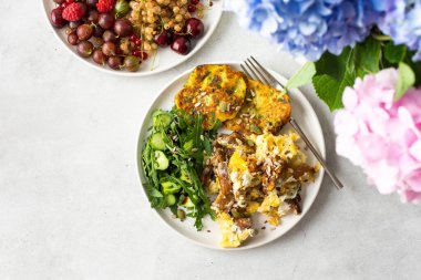 Sağlıklı kahvaltı, kızarmış mantarlı omlet roka, roka salatası, salatalık ve çeşitli tohumlar, kızarmış kabak gözlemesi, böğürtlenli bir tabak ve bir buket ortanca.