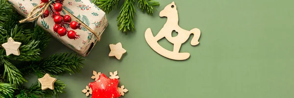 Christmas holiday banner, gift boxes with rowan twig and wooden stars, candy staff and rocking horse on a green background, top view