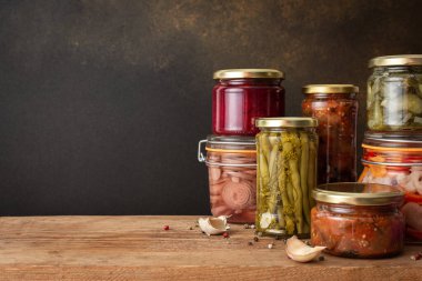 Preserving vegetables for the winter, canned vegetables in jars on a wooden table against a brown wall, pickled or fermented vegetables, copy space