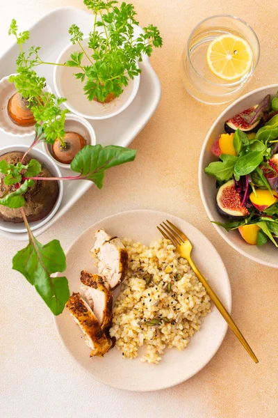 Delicious hearty lunch, brown rice with baked chicken breast and seeds, mixed salad with figs and peach, sprouted carrot and beet tops