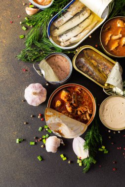 Baharat ve bitkilerin arasında farklı teneke kutular, kahverengi bir arka planda konserve somon ve uskumru, sprat ve sardalya, ton balığı ve ringa balığı ve balık ezmesi.