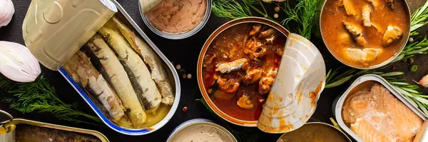 Baharat ve otların arasında konserve balık konserveleri, konserve somon ve uskumru, sprat ve sardalya, ton balığı ve ringa balığı ve balık ezmesi, üst görünüm.