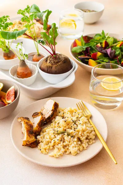 Delicious hearty lunch, brown rice with baked chicken breast and seeds, mixed salad with figs and peach, sprouted carrot and beet tops