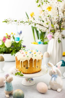 Paskalya Evi 'nin içi, vazonun arka planında yumurtalar, çiçek açan kiraz dalları ve buketler dolusu çiçekler, sevimli tavşanlar olan Paskalya pastası.