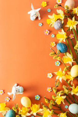 Turuncu arka planda doğal boyanmış Paskalya yumurtaları, sarı nergisler ve tavşanlar, Mutlu Paskalyalar.