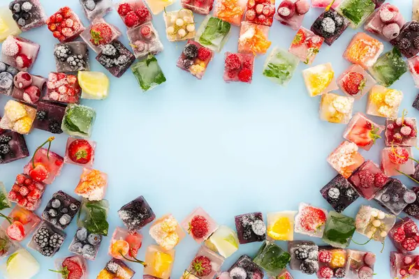 Frame of ice cubes with frozen berries and fruits and mint on blue background