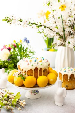 Paskalya Evi 'nin içi, vazonun arka planında yumurtalar, çiçek açan kiraz dalları ve buketler dolusu çiçekler, sevimli tavşanlar olan Paskalya pastası.