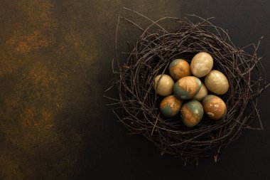 Cosmic Easter eggs in a nest on a brown background, top view, copy space