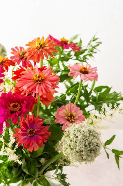 Renkli Zinnia buketi, soğan ve nane filizi, duvarın yanındaki masada bir buket çiçek, çiçeklerle süslenmiş ev dekorasyonu.