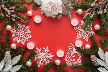 Kırmızı Noel arkaplanı, köknar dalları, pembe Noel ağacı oyuncakları, kar taneleri ve mumlar.