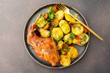 Çok lezzetli bir akşam yemeği, patates ve havuçlu fırında tavşan, içinde yemek olan bir sehpa.