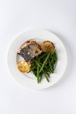 Bu lezzetli yemek, soğanlı ve yumuşak uskumrulu fırında yeşil fasulye içeriyor. Beyaz arka planda servis edilen tabakta sağlıklı bir yemek sunuyor. 