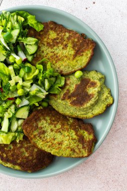Kabak ve brokoli krepleri salatalık, taze bezelye ve turptan oluşan karışık bir salata ile servis ediliyor. Bu sağlıklı vejetaryen yemeği hem lezzetli hem de besleyicidir.