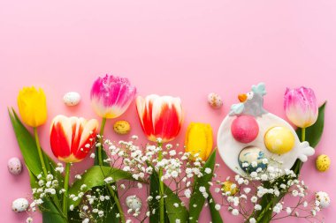 İlkbahar Paskalya arkaplanı, çok renkli Paskalya yumurtaları ve pembe arka planda çigila olan laleler, kopyalama alanı.