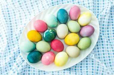 Mavi masa örtüsü üzerinde oval bir tabakta çok renkli Paskalya yumurtaları, üst manzara, mutlu Paskalya tatili.