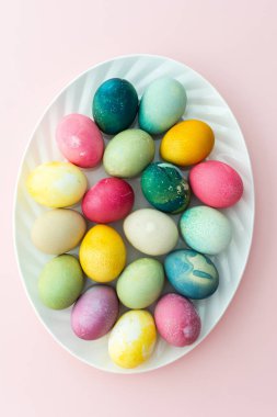 Pembe arka planda oval bir tabakta çok renkli Paskalya yumurtaları, üst manzara, mutlu Paskalya tatili.
