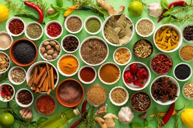 Yumuşak yeşil bir arka planda sergilenen taze kokulu baharat ve bitkilerden oluşan renkli bir karışım, parlak bir mutfak özünü yakalıyor.