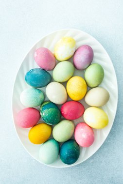 Mavi arka planda oval bir çanakta çok renkli Paskalya yumurtaları, üst manzara, mutlu Paskalya tatili.