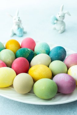 Mavi arka planda dekoratif tavşanlarla oval bir tabakta çok renkli Paskalya yumurtaları, Mutlu Paskalya tatilleri.