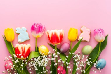 Bahar Paskalya arkaplanı, dekoratif tavşanlı çok renkli Paskalya yumurtaları ve pembe arkaplanlı laleler, kopyalama alanı.