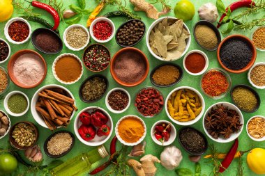 Yumuşak yeşil bir arka planda sergilenen taze kokulu baharat ve bitkilerden oluşan renkli bir karışım, parlak bir mutfak özünü yakalıyor.