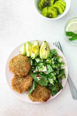 Kinoa pirzolası, avokado ve turpla karışık salata, limonlu kivi ve su, lezzetli, sağlıklı kahvaltı, vejetaryen yemek tabağı.