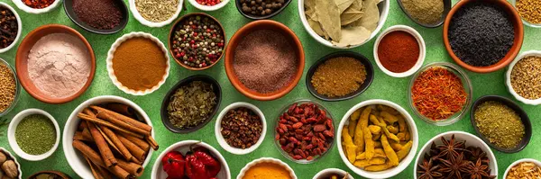 Renkli baharatlar ve bitkiler narin yeşil bir arka planda sergilenmiş, canlı doğal bir görünüş için tazeliklerini ve kokularını vurguluyorlar.