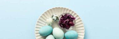 A plate holds several blue-painted Easter eggs and a couple of small patterned eggs, creating a festive atmosphere for the holiday celebration, small bowl of red cabbage, how to dye eggs blue, banner