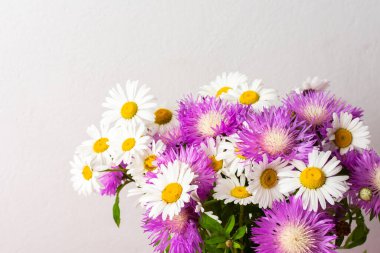 A vibrant bouquet featuring white daisies with yellow centers and purple asters is showcased against a plain background, creating a lovely, cheerful display